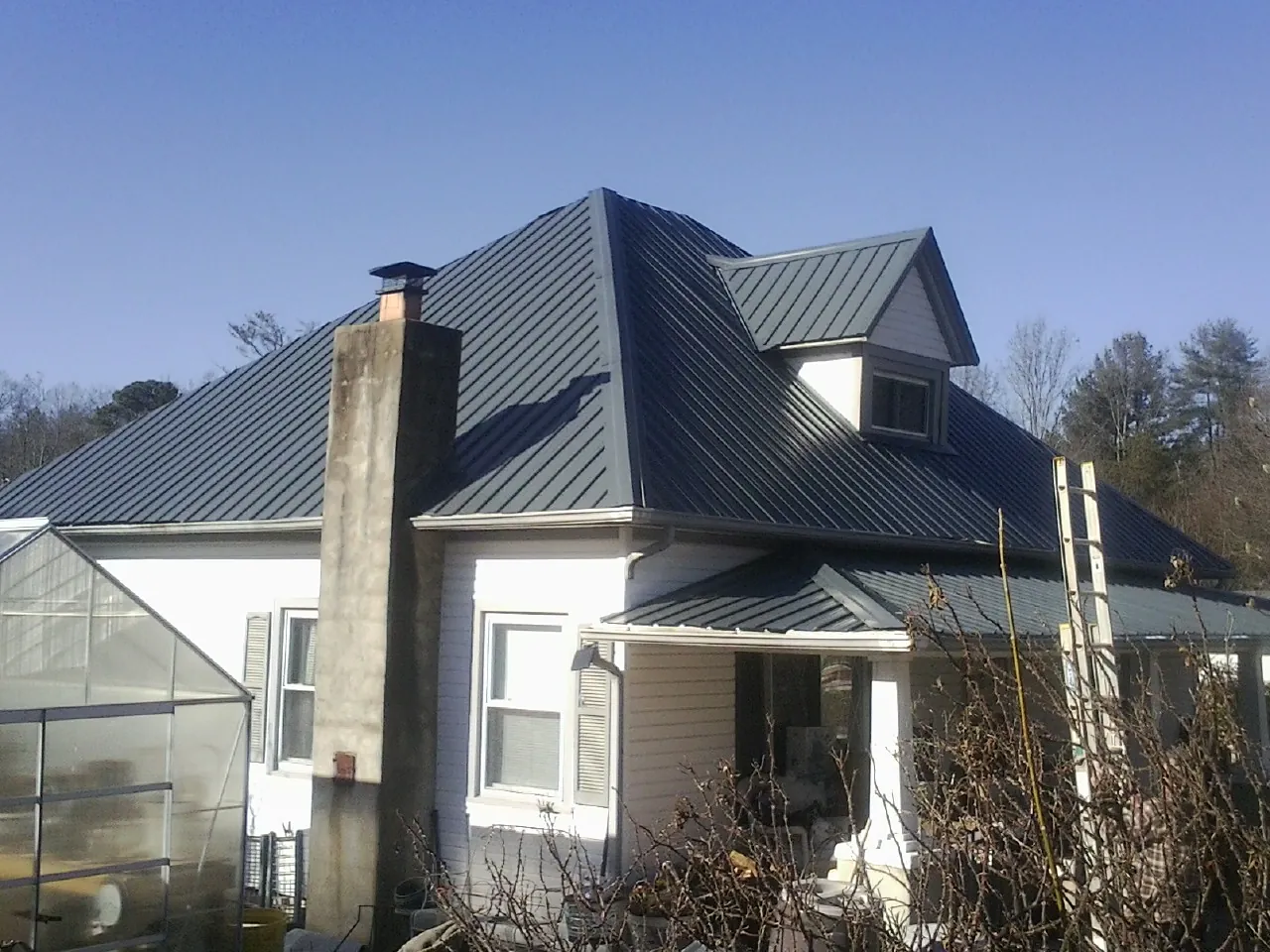 Dark blue standing seam metal roof on a white farmhouse with dormer — Slate & Tile Roof Repair by Roofing Brothers in East Killingly