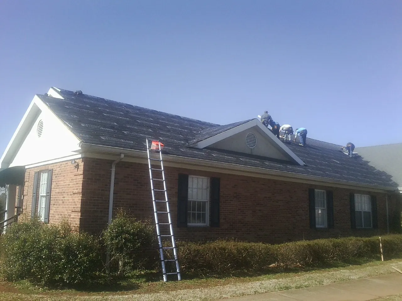 Crew tearing shingles off a brick ranch roof with a ladder set — Emergency Roof Repair work by our crew in East Killingly
