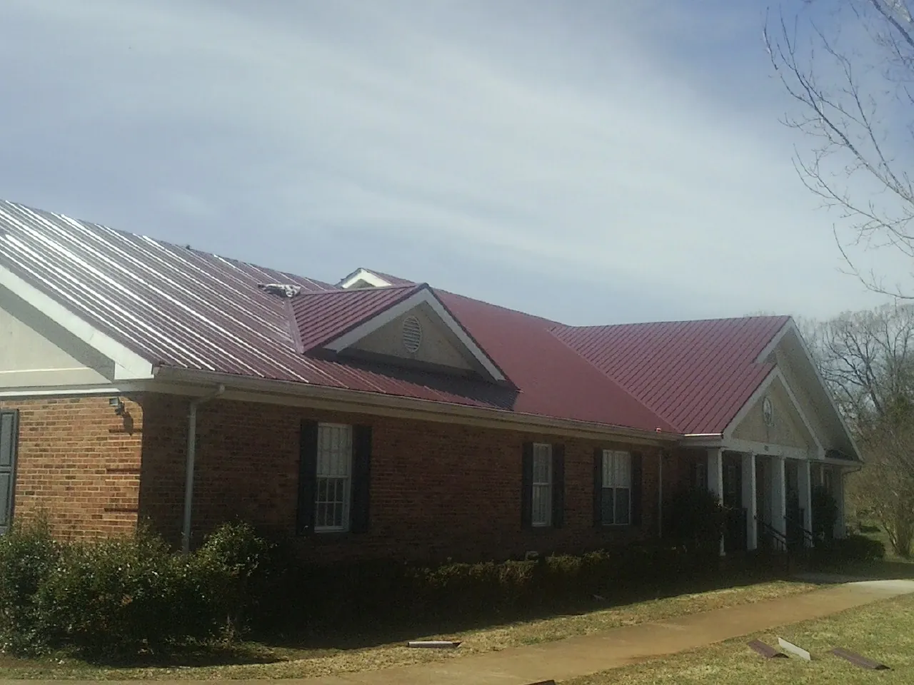 Red metal roof with gabled entries on a long brick building, from a Hail Damage Roof Repair job in East Killingly