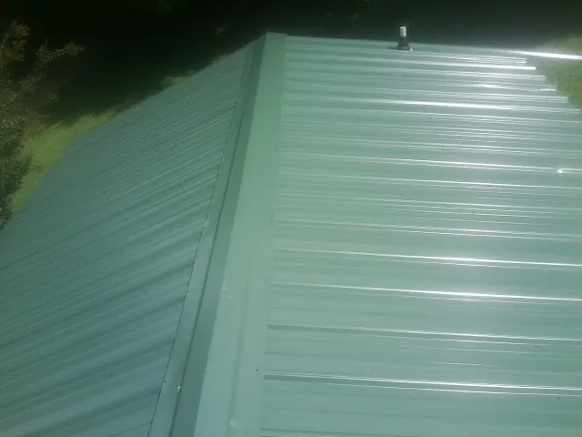 New green metal panels meeting at the ridge of a roof — Flat Roof Repair work by our crew in East Killingly