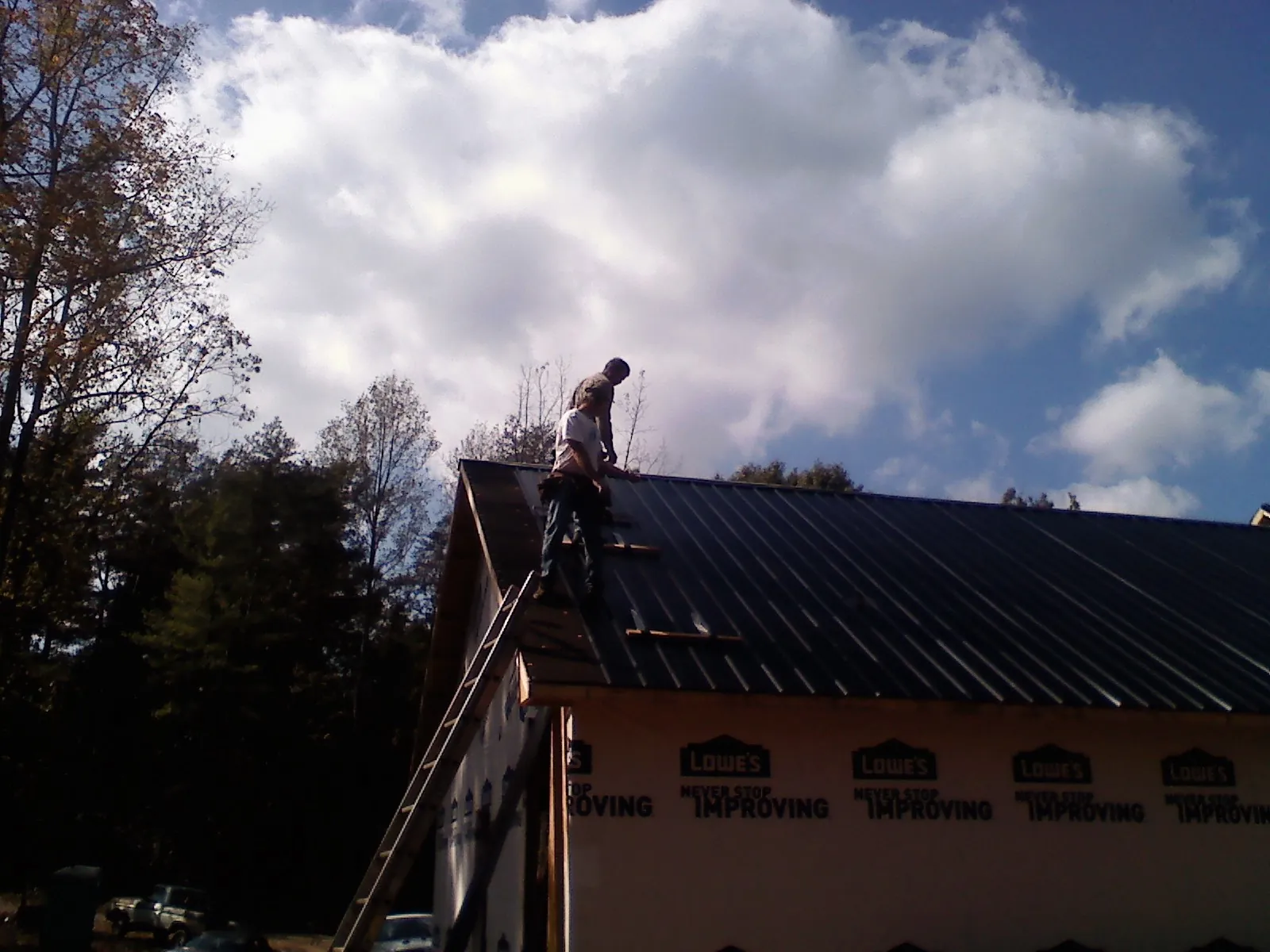 Roofer fastening dark metal panels high against a cloudy sky, from a Roof Inspection job in East Killingly