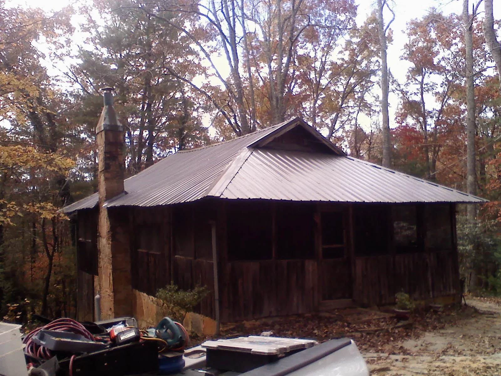 Brown metal hip roof on an old cabin with a stone chimney in East Killingly