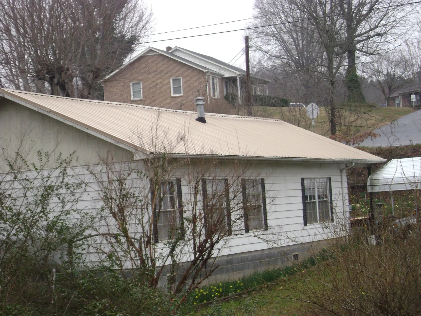 Tan metal roof on a white sided house set into a hillside — Commercial Roofing by Roofing Brothers in East Killingly